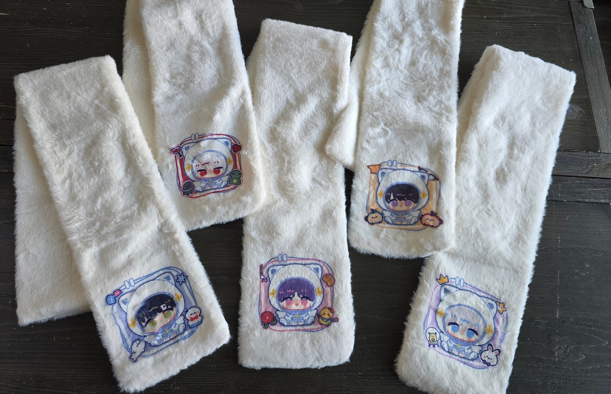 Set of white scarfs with printed designs of sylus, rafayel, caleb, zayne and xavier on a wooden surface